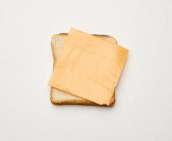fatias quadradas de pão torrado feito com farinha de trigo branca e uma fatia de queijo cheddar por cima. fundo de mesa branco foto