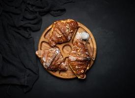 croissants assados em uma placa de madeira preta polvilhada com açúcar de confeiteiro, vista superior foto