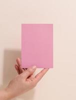 mão feminina segurando papel rosa vazio em um fundo bege. copiar e colar imagem ou texto, fechar foto