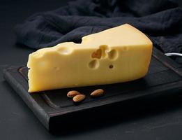 pedaço triangular de queijo maasdam em uma placa de madeira marrom foto