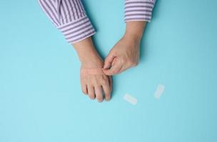 mão feminina e gesso adesivo médico marrom para o tratamento de lesões e cortes na pele, fundo azul foto