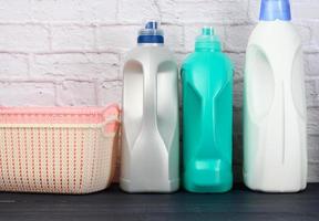 garrafas com detergente líquido e cestas de roupa vazias de plástico em uma mesa de madeira azul foto