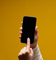 mão feminina segurando smartphone com tela preta em branco sobre fundo amarelo foto