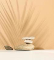 pilha de pedras redondas ee a sombra de uma folha de palmeira sobre um fundo bege. cena para demonstração de produtos cosméticos, publicidade