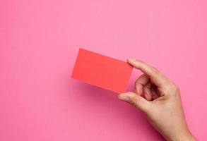 mão feminina segurando papel vermelho vazio em um fundo rosa. copiar e colar imagem ou texto foto
