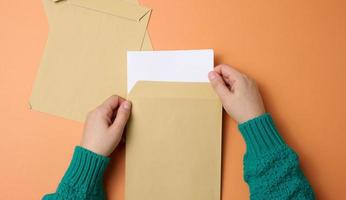 mão feminina segura envelopes de papel em um fundo laranja, vista superior. correspondência foto