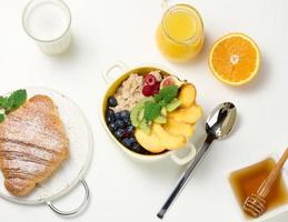 prato com aveia e frutas, meia laranja madura e suco espremido na hora em uma jarra de vidro transparente, mel em uma tigela sobre uma mesa branca. café da manhã saudável foto