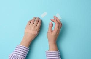 mão feminina e gesso adesivo médico marrom para o tratamento de lesões e cortes na pele, fundo azul foto