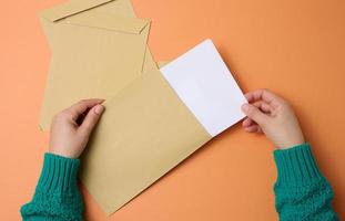 mão feminina segura envelopes de papel em um fundo laranja, vista superior. correspondência foto