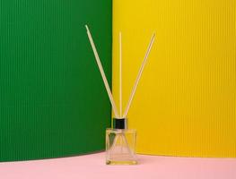 frasco de vidro e varas de madeira, lâmpada de aroma em fundo colorido foto