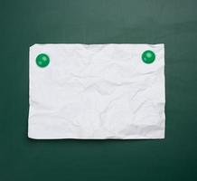 folha de papel a4 amassada branca em branco pendurada em um quadro magnético verde. lugar para inscrição foto