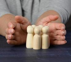 mãos femininas protegem figuras de madeira de homens. conceito de proteção e orientação. preservação da equipe em momentos de crise foto