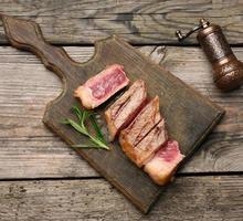 filé de carne frita fatiado contra filé de Nova York em uma tábua de corte de madeira, grau de cozimento raro foto