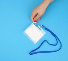 mão feminina segura distintivo de plástico transparente em um cordão azul sobre fundo azul foto