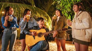 retrato de grupo asiático feliz de amigos se divertindo com música jantando e bebendo juntos ao ar livre - grupo de amigos felizes brindando cervejas - pessoas, comida, estilo de vida de bebida, conceito de celebração de ano novo. foto