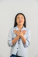 retrato de uma jovem mulher asiática feliz na camisa azul mostrando seu coração cheio de amor e segurando as mãos em seu peito isolado no fundo branco foto