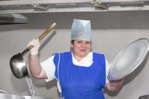 uma mulher cozinha em uma cozinha industrial com uma grande concha entre panelas de metal. cozinheiro do hospital foto