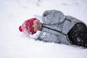 o menino deita na neve no inverno e ri. foto