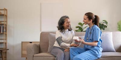 mulher sênior feliz tendo sua pressão arterial medida em um lar de idosos por seu cuidador. enfermeira feliz medindo a pressão arterial de uma mulher sênior na sala de estar foto