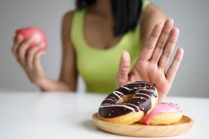 as mulheres empurram o prato de donuts que é uma mistura de gordura trans. e escolha segurar a maçã. não coma junk food. conceito de dieta foto