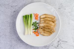 peito de frango cozido no vapor em um prato branco com cebolinhas e cenouras foto