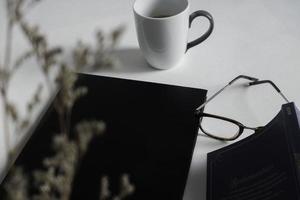 vista superior do espaço de trabalho mínimo com tela em branco, livro, uma xícara de café, óculos, caneta na mesa de cor branca. foto