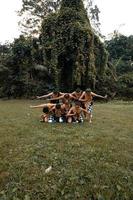 um grupo de indonésios dançando pose em um terno dourado enquanto usava maquiagem na grama verde foto