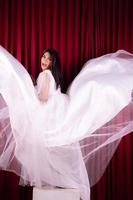 linda mulher asiática de pé em um vestido de noiva voador na frente do fundo vermelho foto