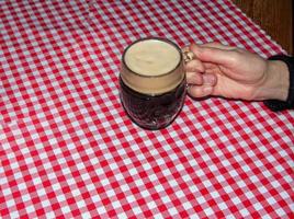 uma caneca de cerveja em uma mesa coberta com uma toalha xadrez vermelha.