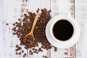 grãos de café e uma xícara de café na mesa branca foto