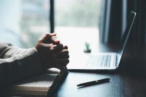 conceito de tecnologia online cristã. mãos orando de cristão com laptop de computador digital, igreja ao vivo online para o culto de domingo. a mulher católica asiática está lendo o livro da bíblia sagrada e o estudo online. foto