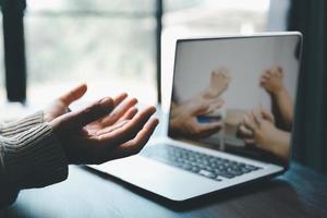 conceito de tecnologia online cristã. mãos orando de cristão com laptop de computador digital, igreja ao vivo online para o culto de domingo. a mulher católica asiática está lendo o livro da bíblia sagrada e o estudo online. foto