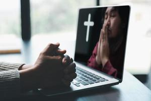 conceito de tecnologia online cristã. mãos orando de cristão com laptop de computador digital, igreja ao vivo online para o culto de domingo. a mulher católica asiática está lendo o livro da bíblia sagrada e o estudo online. foto