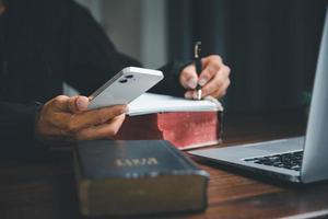 conceito de tecnologia online cristã. mãos orando de cristão com laptop de computador digital, igreja ao vivo online para o culto de domingo. o homem católico asiático está lendo o livro da bíblia sagrada e o estudo online. foto