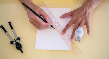 mão feminina usando uma régua com o lápis se preparando para desenhar e esboçar no papel branco vazio. foto