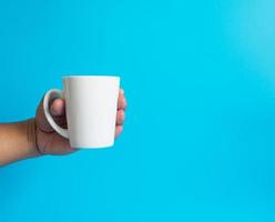 mão de homem segurando uma xícara de café branco, cheia de café preto quente americano, sem açúcar sem leite, pronto para beber, refrescante. aroma acordado fresco para trabalhar colocado em um fundo azul isolado foto