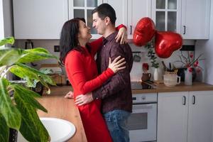 homem e mulher apaixonados namoram em casa na cozinha abraços felizes. dia dos namorados, casal feliz, história de amor. ninho de amor, moradia para família jovem foto