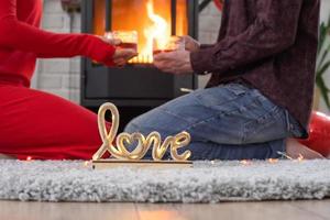 homem e mulher apaixonados em casa estão sentados perto do fogão da lareira com fogo aceso em um tapete aconchegante. dia dos namorados, casal feliz, história de amor, relacionamentos foto