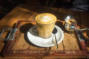 café com latte art em chapa branca e bandeja de madeira à luz do sol foto