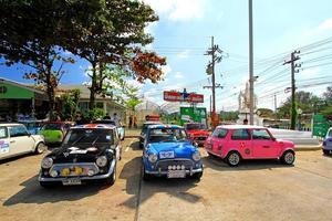 nakhonratchasima, tailândia - 31 de janeiro de 2023, muitos belos carros austin mini cooper estacionando na rua com árvore e fundo de céu azul. transporte, carro clássico ou antigo e conceito de veículo foto