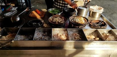 a mão do homem cozinhando bak kut quente na panela para venda com a luz do sol pela manhã no mercado de comida - cozinha, preparação e conceito de serviço foto