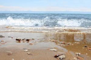 praia desfocada com onda turva e areia molhada com seixo no céu azul. mar, fundo do oceano. férias ao ar livre e viagens conceito de aventura de férias foto