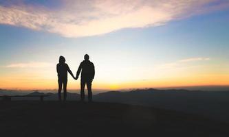 silhueta de um casal na montanha, um jovem casal romântico desfruta de uma bela vista do pôr do sol sobre as montanhas, amor, dia dos namorados. foto