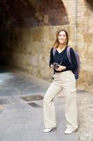 senhora alegre com câmera fotográfica sorrindo na rua durante a viagem de turismo foto