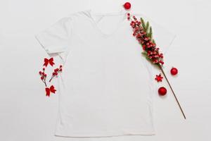 feche a camiseta branca modelo em branco com espaço de cópia e o conceito de férias de natal. t-shirt de maquete de vista superior e decorações vermelhas de feriados em fundo branco. feliz ano novo acessórios. roupa de natal foto