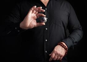 homem de camisa preta segura uma bola de pedra para rituais religiosos, meditações foto