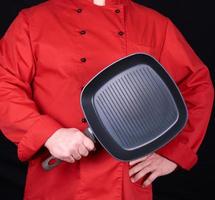cozinhe de uniforme vermelho segurando uma frigideira preta quadrada vazia foto