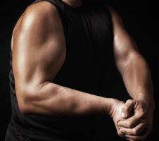 homem adulto com uma figura esportiva em roupas pretas esticou os músculos dos braços foto