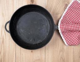 frigideira redonda preta vazia com alça de madeira e guardanapo de cozinha vermelho foto