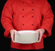 cozinheiro de uniforme vermelho segura em suas mãos uma pilha de pratos vazios brancos redondos, pretos foto